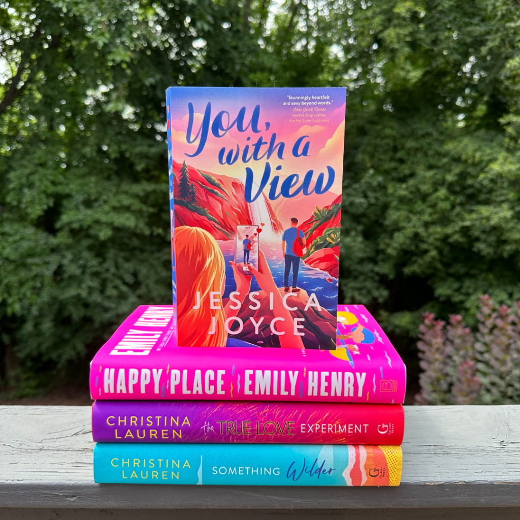 Four romance novels stacked on a railing with trees in the background for National Book Lovers Day